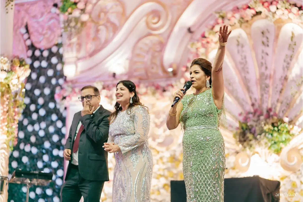 Anchor Anu Manocha hosting a wedding sangeet in Delhi, mic in hand and arm raised