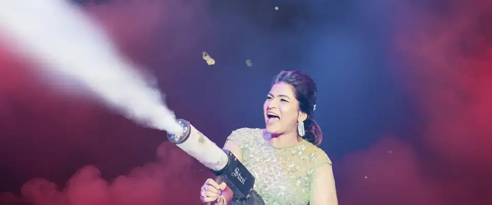 Anchor Anu Manocha laughing on stage with a confetti CO2 jet at a celebration party in Delhi NCR