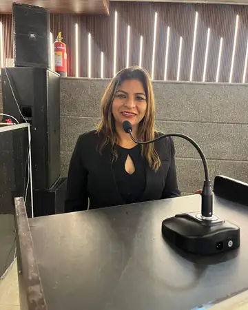 Anu Manocha at a conference lectern with a gooseneck mic