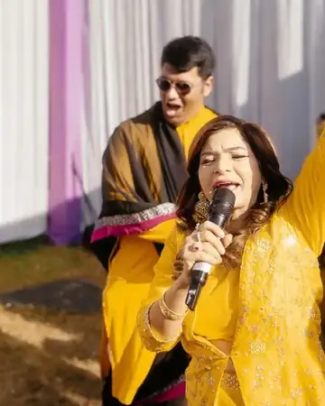 Anu Manocha in a yellow outfit singing with guests at a haldi ceremony