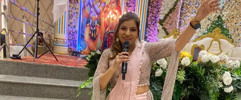 Anu Manocha in a pink saree hosting a function with a Radha-Krishna backdrop