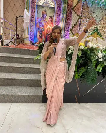 Anu Manocha in a pink saree hosting a function with a Radha-Krishna backdrop