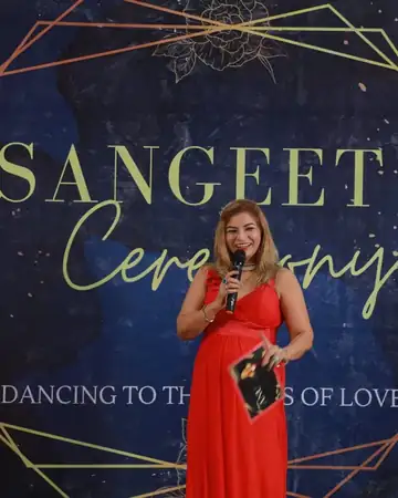 Anu Manocha with mic and script at a Sangeet Ceremony