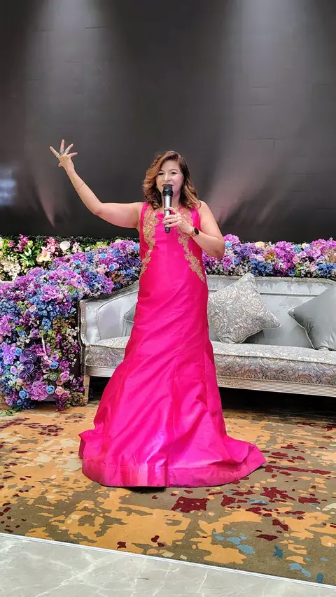 Anu Manocha in a pink gown with arm raised on a wedding stage