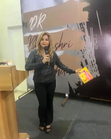 Anu Manocha on stage holding a book at a speaker event